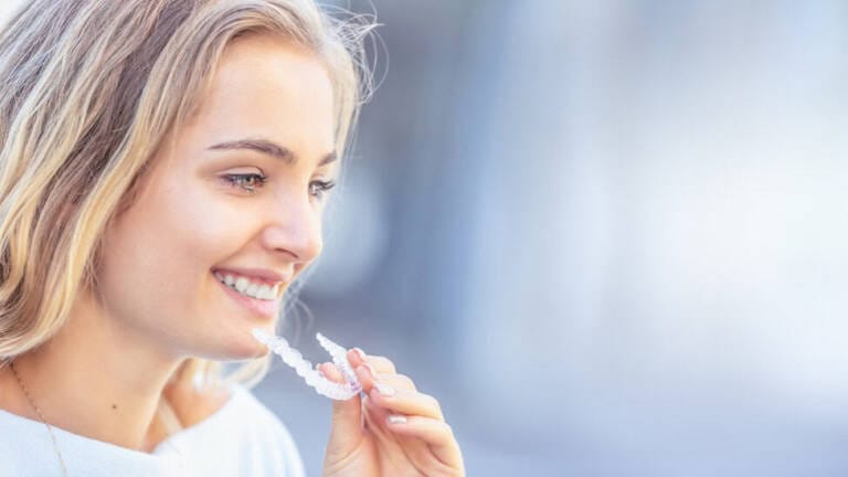 Smiling woman holding an Invisalign clear aligner designed to fit a crowned tooth