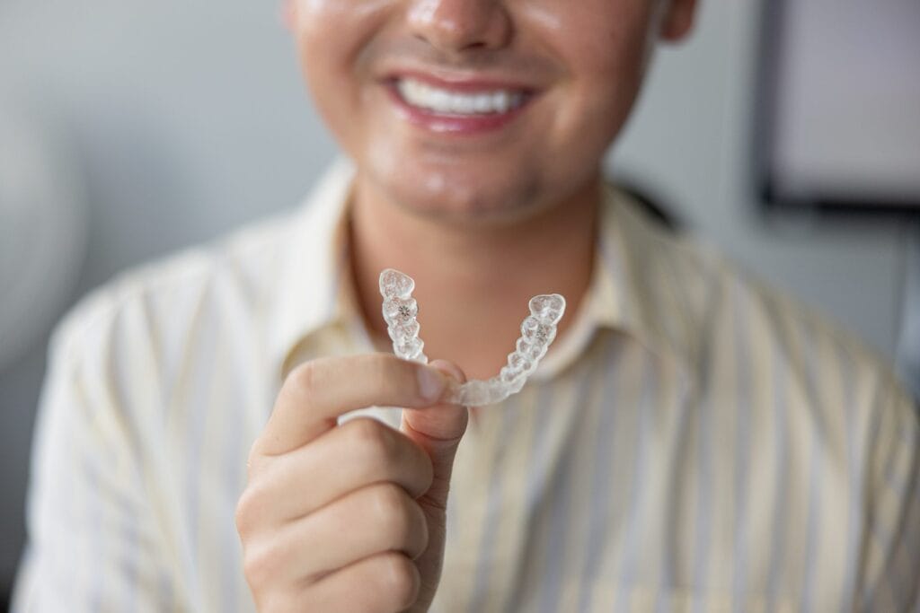 Smiling patient holding an Invisalign clear aligner
